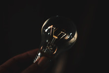 Close-up Of Hand Holding Light Bulb Against Black Background
