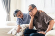 © Kawee - Asian senior old man having headache stress problem put hand on temple sitting on sofa at home. Elder wife sit beside consoling husband put hug, put hand on shoulder. Make comfort talking to relax him