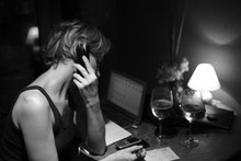 Woman Listening To Mobile Phone While Writing On Paper At Home