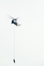 Low Angle View Of Army Soldiers Hanging On Rope Attached To Helicopter For Rescue Mission