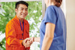 © DragonImages - Smiling handsome Asian service worker shaking hand of female customer opening house door