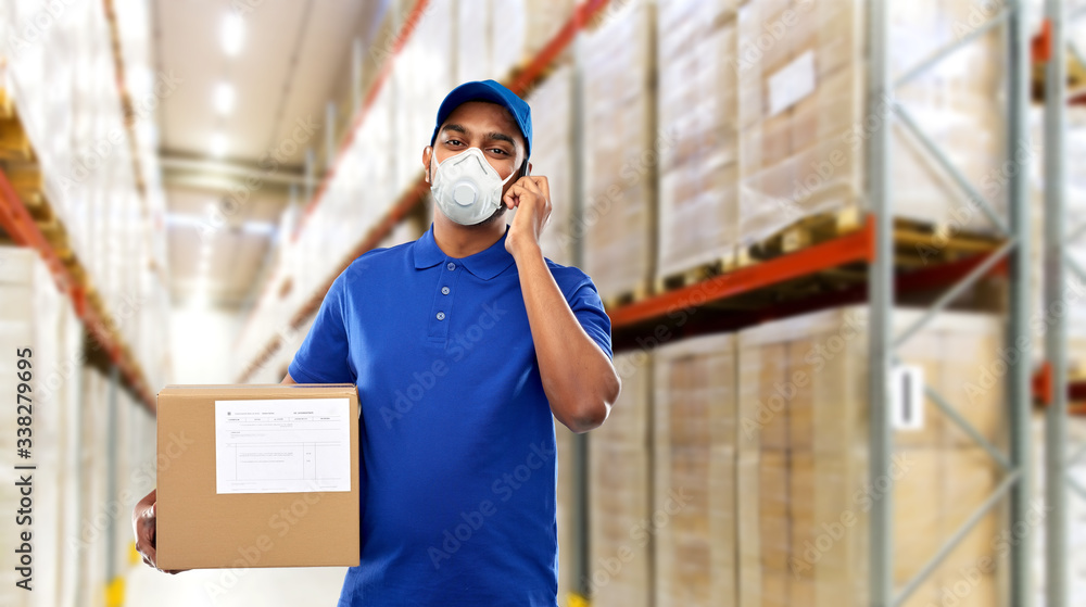 health, safety and pandemic concept - happy indian delivery man with smartphone and parcel box wearing face protective mask for protection from virus over warehouse background - obrazy, fototapety, plakaty 