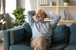 © fizkes - Smiling mature man dreaming, relaxing on cozy couch alone, happy older senior male with hands behind head sitting resting on sofa in living room, looking in window, thinking about good future
