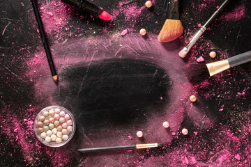 A make-up brush with crushed cosmetics, brushes, and lipstick on a black background, with a place for text, a beauty frame for a makeup school