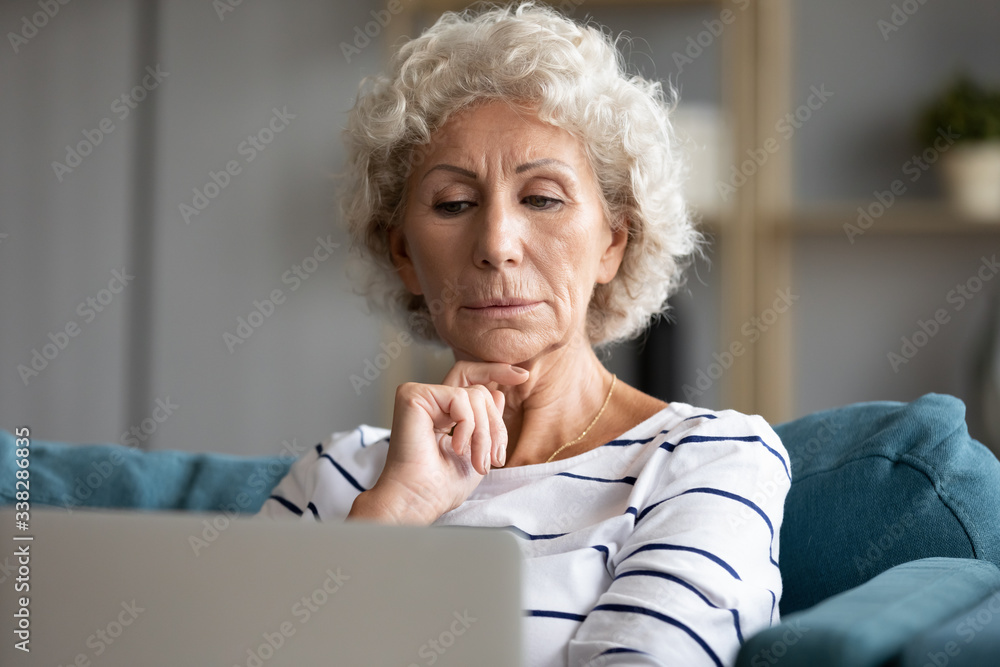 Serious pensive older woman looking at laptop screen, reading email or ...