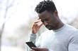 © PheelingsMedia - Worried black man reading bad news on phone at park
