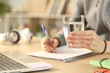 © PheelingsMedia - Student hands holding glass of water studying with notebook