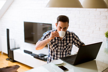 Wall Mural - Young man sitting on kitchen desk at home and using laptop and drinking coffee