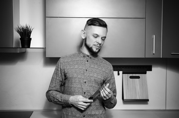 Sticker - attractive bearded man examines a knife in his hands in the modern kitchen