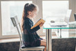 © alexngm - School girl  is studying online. Home schooling. Distance education. Little girl is reading book.