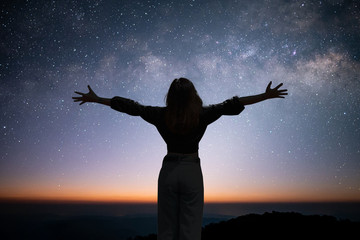 Wall Mural - Silhouette of young traveler open arm and watching the star and milky way on the top of the mountain and enjoying with beautiful view of the stars before sunrise on top of the mountains.