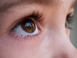 Fototapeta  - Close up image of a girl's brown eye looking out of a window 