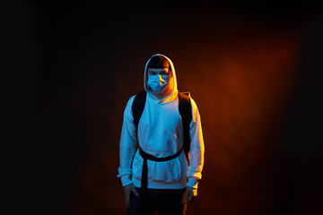 delivery man in white clothes in medicine mask with a yellow backpack on a black background with red light