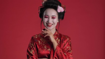 Canvas Print - A happy positive young geisha woman in traditional japanese kimono is laughing isolated over red background