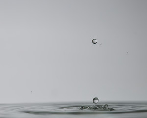 Gotas de agua cristalina chapoteando en una superfície de agua calmada y formando ondas circulares