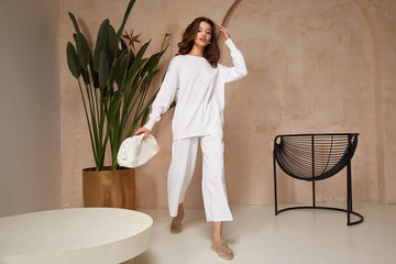 Wall Mural - Beautiful sexy brunette woman face cosmetic makeup tanned skin wear fashion clothes style white knitted suit shoes accessory bag interior furniture armchair journey summer flowerpot palm boho.