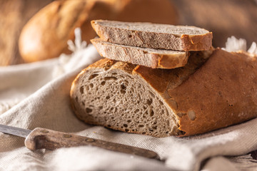 Two slices of freshly baked bread placed on top of the loaf and a linen cloth with a knife on a side