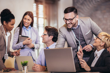 Smiling young manager helping senior worker with computer work in office, mentor teacher training, happy older employee at workplace.