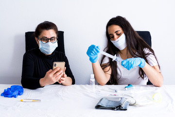 Nurse preparing syringe in hospital to treat patient infected with virus. Patient looking at her cell phone. Vaccine prepared. Coronavirus pandemic.