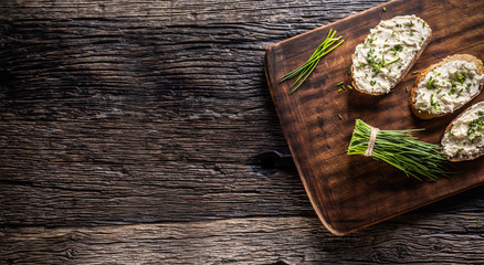 Wall Mural - Banner of bread slices with a dairy product spread, freshly cut chives placed on a dark brown cutting board and vintage background