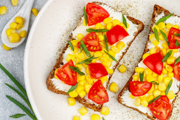 Wall Mural - Delicious rye bread sandwiches with cream cheese or ricotta, corn, cherry tomato and green onion close-up. Healthy Breakfast in a white plate on a gray concrete background. Selective focus