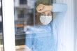 Leinwandbild Motiv Young woman in quarantine wearing a mask and looking through the window