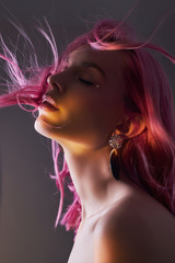 Wall Mural - Art beauty portrait of a woman with pink hair, creative coloring. Bright colored highlights and shadows on the face, a girl with jewelry. Dyed hair in the wind