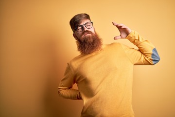 Wall Mural - Handsome Irish redhead man with beard wearing glasses over yellow isolated background stretching back, tired and relaxed, sleepy and yawning for early morning