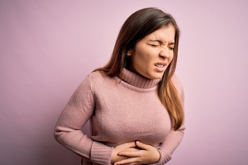 Canvas Print - Beautiful young woman wearing turtleneck sweater over pink isolated background with hand on stomach because nausea, painful disease feeling unwell. Ache concept.