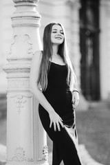 Wall Mural - girl with long hair in a black dress poses near the column on bl