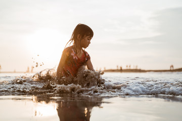 asian little girl sitting on sand in the beach while playing water on a nice beach