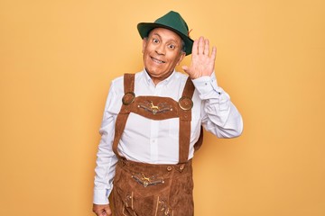 Sticker - Senior grey-haired man wearing german traditional octoberfest suit over yellow background Waiving saying hello happy and smiling, friendly welcome gesture