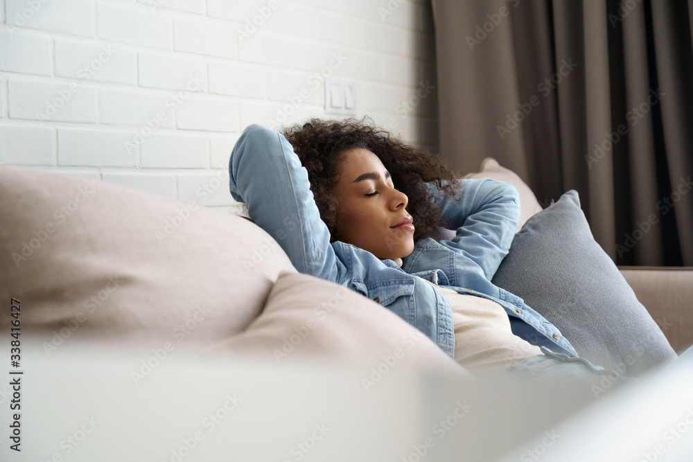 Relaxed tired young african american woman napping on comfortable sofa with eyes shut closed. Calm lazy black girl leaning on couch in living room enjoying chill sleeping resting at home concept. - obrazy, fototapety, plakaty 