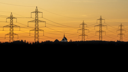 energy system and electricity, panoramic view silhouette of transmission towers and small church during sunset