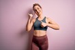 © Krakenimages.com - Young beautiful blonde sportswoman doing sport wearing sportswear over pink background Pointing to the back behind with hand and thumbs up, smiling confident