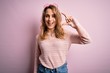 © Krakenimages.com - Young beautiful blonde woman wearing casual sweater and sunglasses over pink background smiling and confident gesturing with hand doing small size sign with fingers looking and the camera. Measure