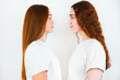 two redheaded young women looking at each other standing sideways on isolated white backgroung