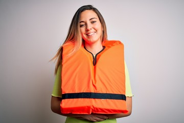 Young beautiful blonde woman with blue eyes wearing orange lifejacket over white background happy face smiling with crossed arms looking at the camera. Positive person.