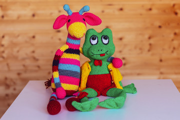 Handmade dolls amigurumi giraffe and frog are sitting close together.