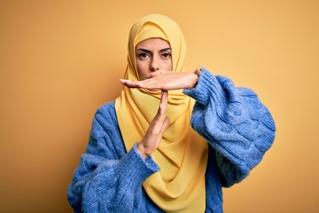 Poster - Young beautiful brunette muslim woman wearing arab hijab over isolated yellow background Doing time out gesture with hands, frustrated and serious face