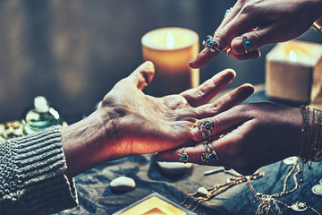 Wall Mural - Fortune teller woman wearing silver rings with turquoise stone and bracelets reads palm lines during fortune telling around candles and other magic accessories. Palmistry and divination