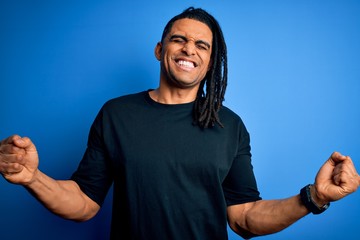 Wall Mural - Young handsome african american afro man with dreadlocks wearing casual t-shirt very happy and excited doing winner gesture with arms raised, smiling and screaming for success. Celebration concept.