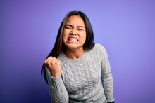 Young Beautiful Asian Girl Wearing Casual Sweater Standing Over Isolated Purple Background Angry And Mad Raising Fist Frustrated And Furious While Shouting With Anger. Rage And Aggressive Concept.