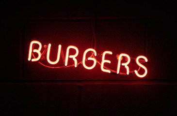 a vintage retro american style neon sign advertising burgers. a dark setting with neon tube lighting