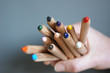 © Leoniek - Hand holding many multi colored pencils against a gray background
