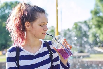 Teen girl holding glass with straw with purple drink in hand