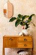 © FollowTheFlow - Retro composition of living room interior with wooden vintage commode, goldpink mirror, plant, rattan basket, plaid, decoration and elegant personal accessories in wabi sabi home decor.