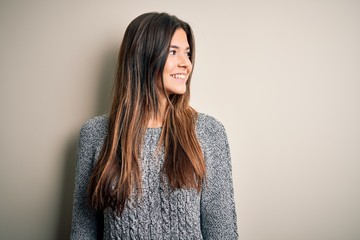 Poster - Young beautiful girl wearing casual sweater standing over isolated white background looking away to side with smile on face, natural expression. Laughing confident.