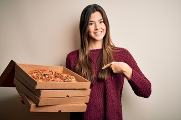 Sticker - Young beautiful girl holding delivery boxes with Italian pizza standing over white background with surprise face pointing finger to himself