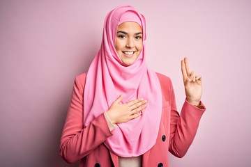 Sticker - Young beautiful girl wearing muslim hijab standing over isolated pink background smiling swearing with hand on chest and fingers up, making a loyalty promise oath